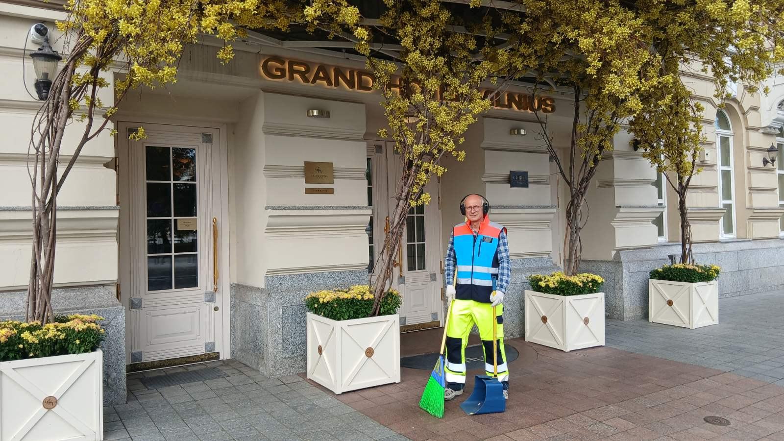 Kiemsargis su šluota ir semtuvėliu prie Grand Hotel Vilnius įėjimo